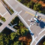 Plano aéreo de drones inspeccionando una carretera rodeada de naturaleza y tecnología analítica.