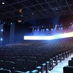 Auditorio moderno con presentaciones tecnológicas y espectadores atentos al evento.