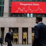 Entre la bruma, un edificio de Wall Street con pantallas mostrando gráficos financieros en rojo.