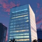 Edificio corporativo moderno iluminado durante el amanecer, con un fondo de cielo despejado.