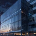 Vista moderna de un edificio de oficinas innovador al anochecer, con iluminación tecnológica.