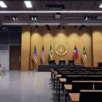Sala de conferencias moderna con representantes de agencias de cooperación firmando un acuerdo frente a laptops y banderas institucionales