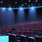 Auditorio moderno con escenografía tecnológica y asistentes observando una presentación con pantallas digitales al fondo