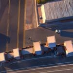 Edificios tecnológicos y camiones de carga junto a robots de manejo logístico, vista aérea al atardecer