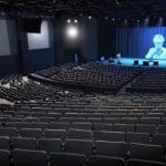 Auditorio lleno durante una conferencia en un festival, con pantallas grandes mostrando gráficos y estadísticas.