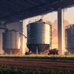 Un campo agrícola con robots trabajando junto a un silo industrial al amanecer