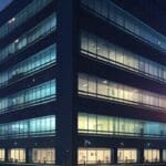 Moderno edificio de oficinas con luces encendidas al atardecer, simbolizando innovación tecnológica.