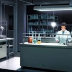 Primer plano de un laboratorio moderno con tubos de ensayo en una mesa de trabajo iluminada y dispositivos médicos de diagnóstico al fondo