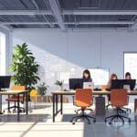 Espacio de coworking moderno con jóvenes desarrolladores frente a pantallas digitales trabajando en prototipos tecnológicos