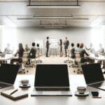 Primer plano de reunión de inversores y emprendedores en un espacio de coworking moderno, con laptops y pizarras.